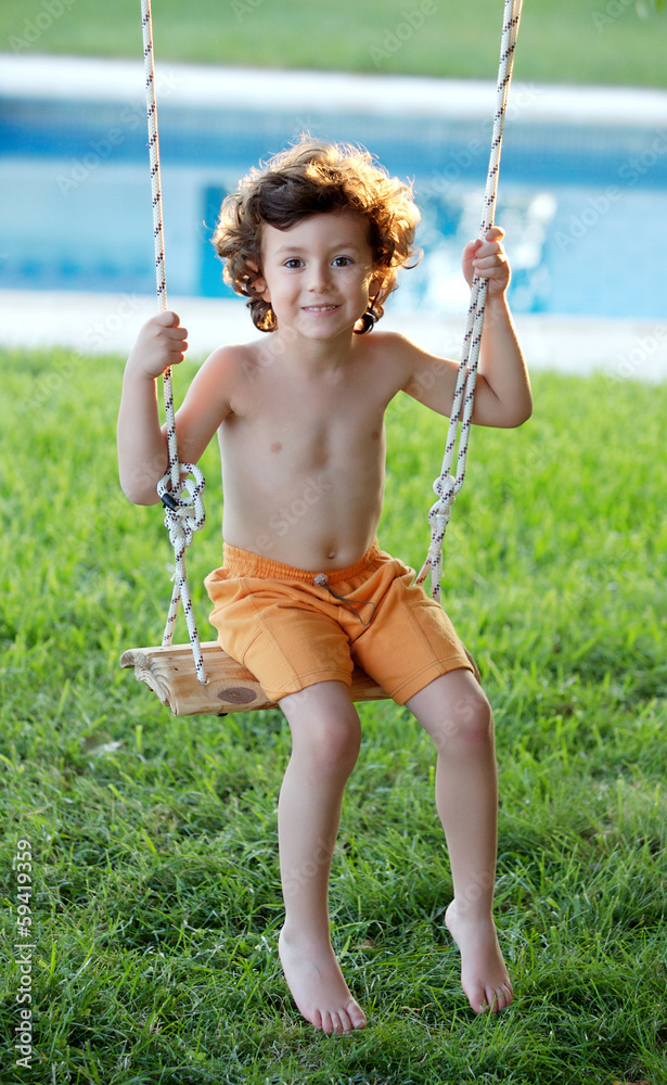 Happy little boy with curly hair sitting on a swing