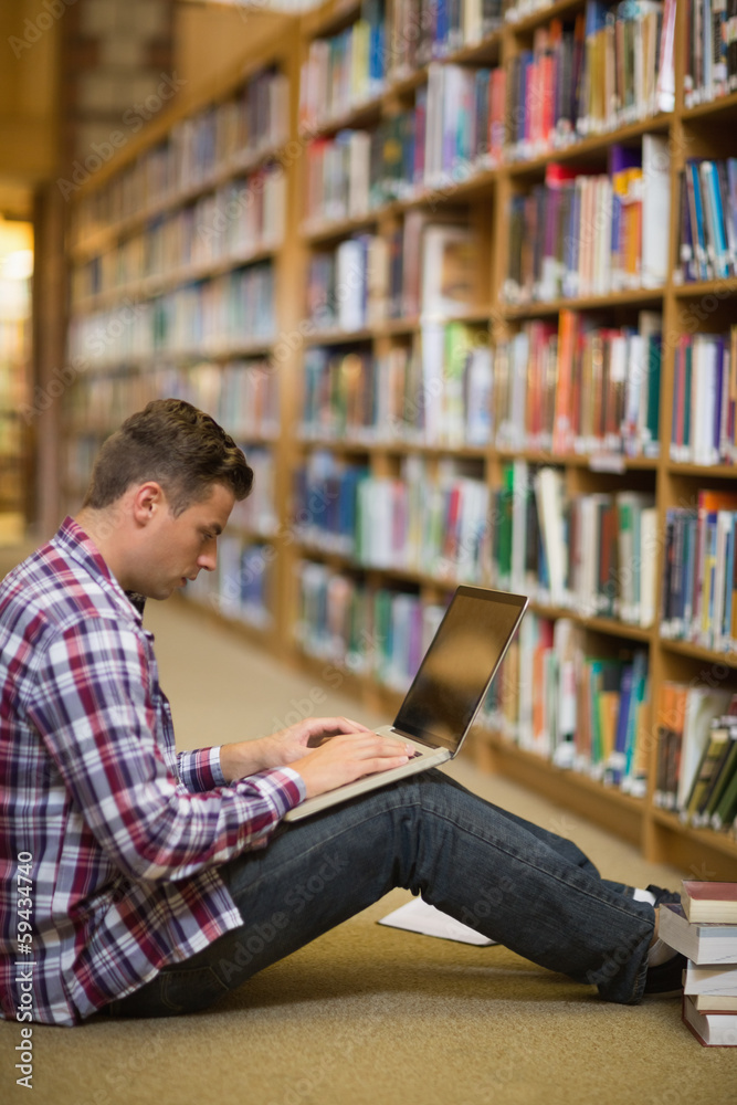 Handsome young student sitting on library floor using laptop Handsome young student sitting on library floor using laptop