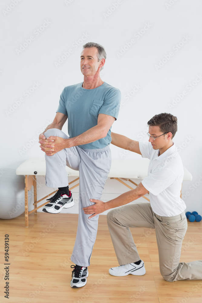 Obraz premium Therapist helping man with stretching exercises in gym hospital