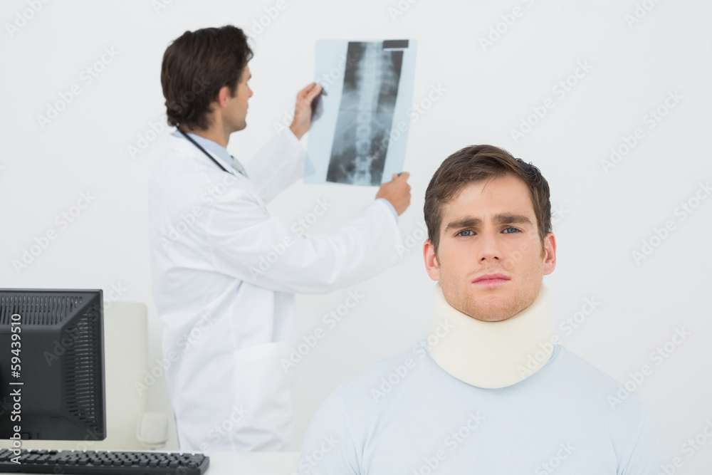 Patient in surgical collar with doctor examining spine x-ray beh