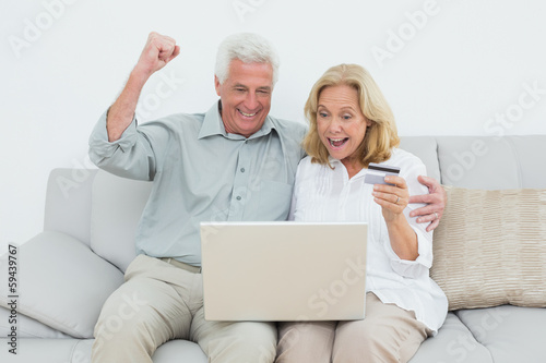 Cheerful senior couple doing online shopping on sofa