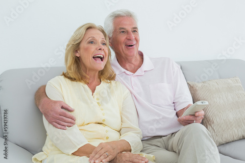 Cheerful senior couple with remote control at home