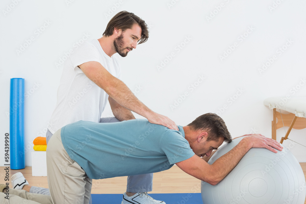 Fototapeta premium Physical therapist assisting young man with yoga ball