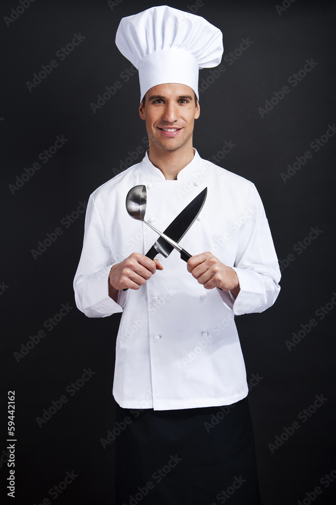 Chef cook against dark background smiling with hat holdinf spoon Chef cook against dark background smiling with hat holdinf spoon