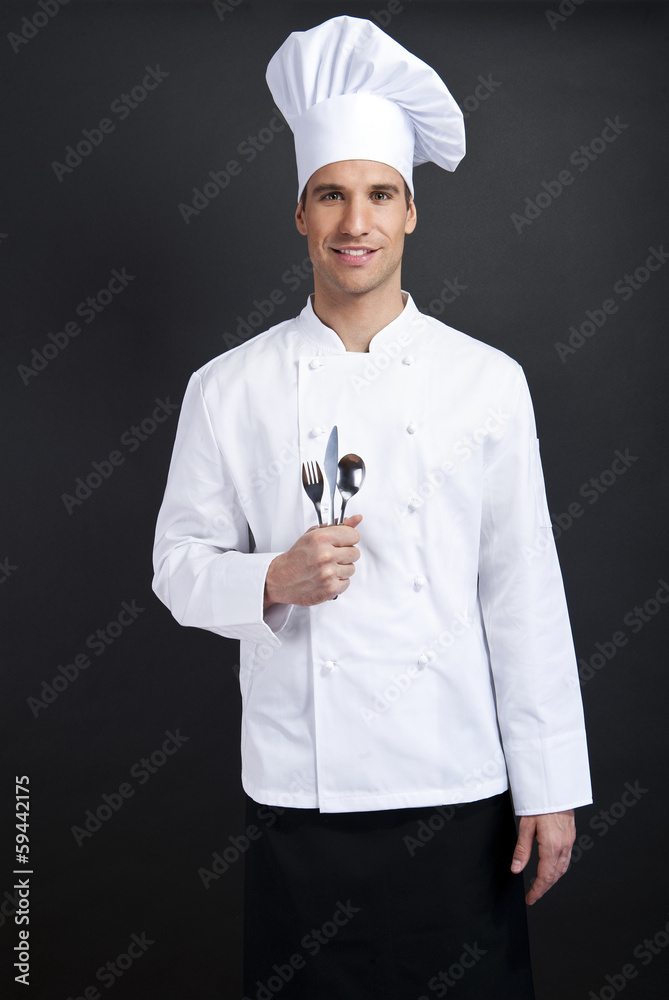 Chef cook against dark background smiling with hat holdinf spoon Chef cook against dark background smiling with hat holdinf spoon