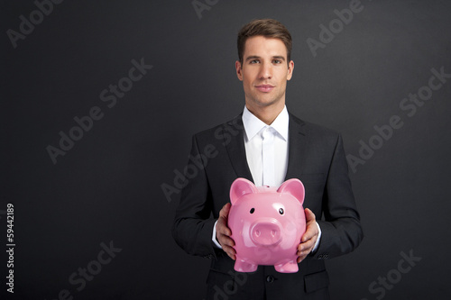 Businessman holding piggy bank against dark background