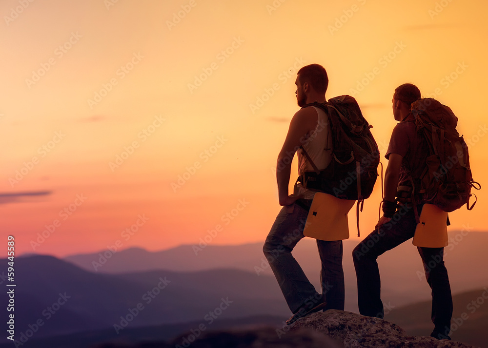 Two hikers enjoying sunrise from top of a mountain