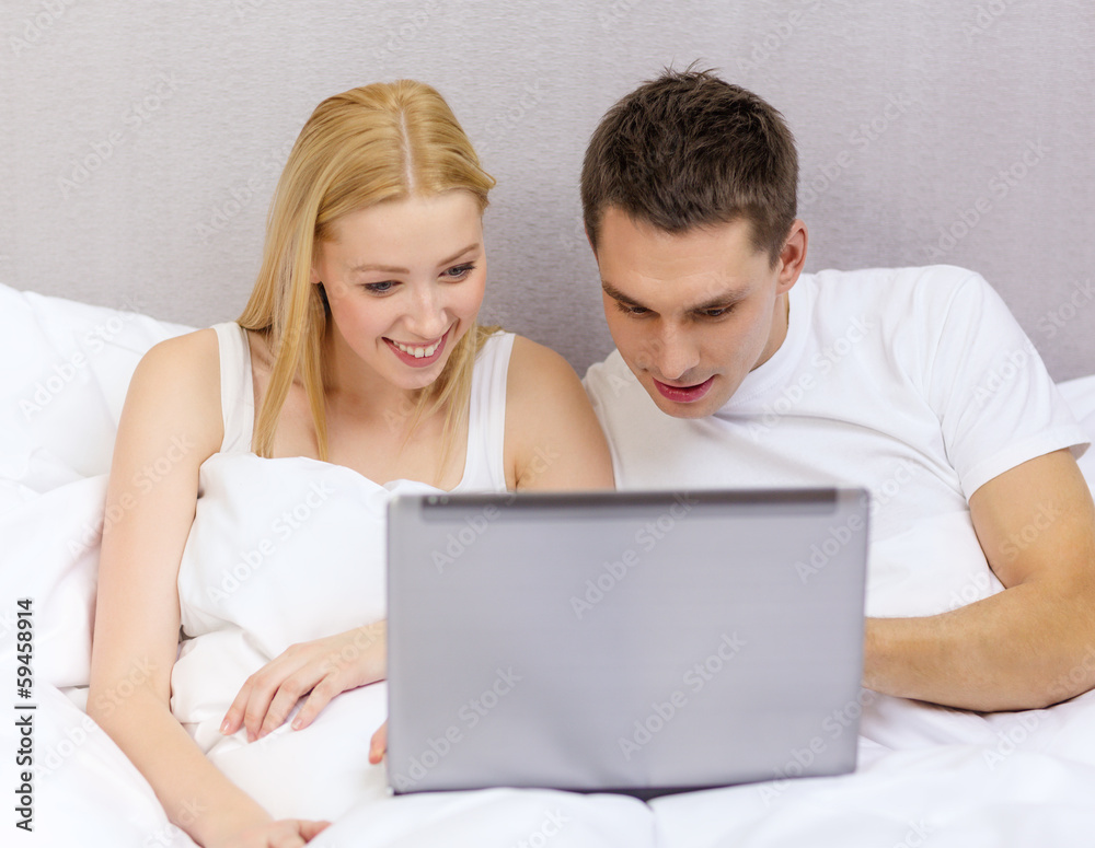 smiling couple in bed with laptop computer smiling couple in bed with laptop computer