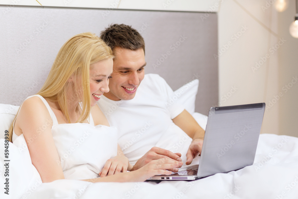 smiling couple in bed with laptop computer smiling couple in bed with laptop computer