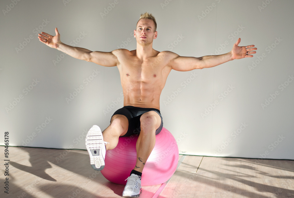 Shirtless young man balancing on fitness ball Shirtless young man balancing on fitness ball