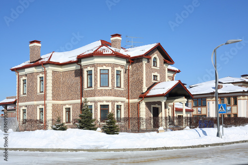 Brown cottage with red roof and drain at frosty and sunny winter