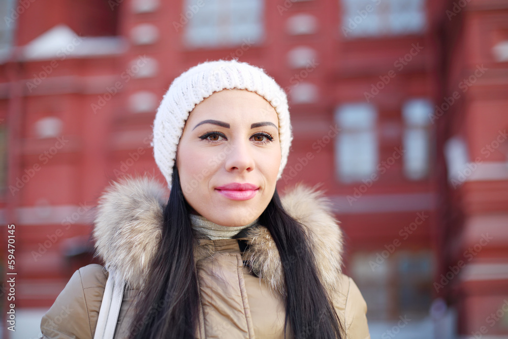 Beautiful woman in white hat stamds near red building at winter Beautiful woman in white hat stamds near red building at winter
