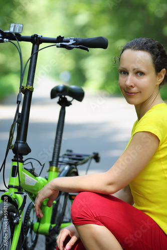 Young woman in sport clothes sits near bike in park at summer