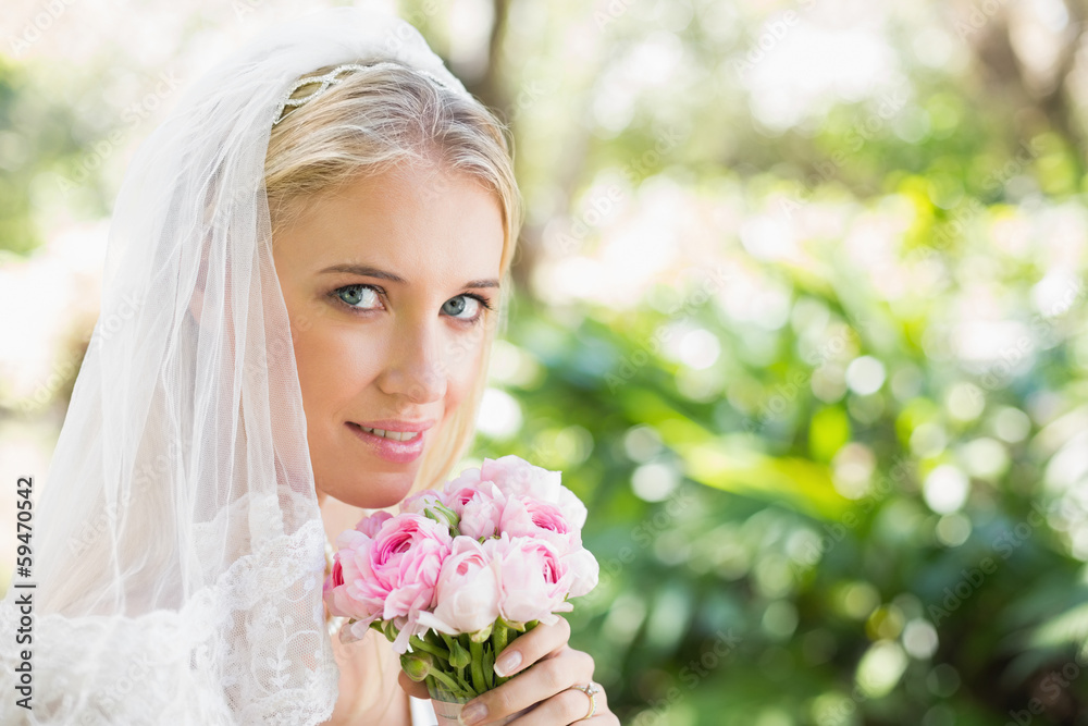 Smiling bride wearing veil holding bouquet looking at camera Smiling bride wearing veil holding bouquet looking at camera