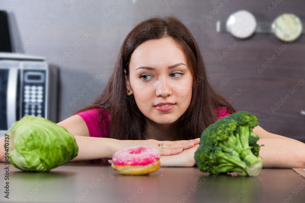 Young woman chooses what to eat vegetables or a cake