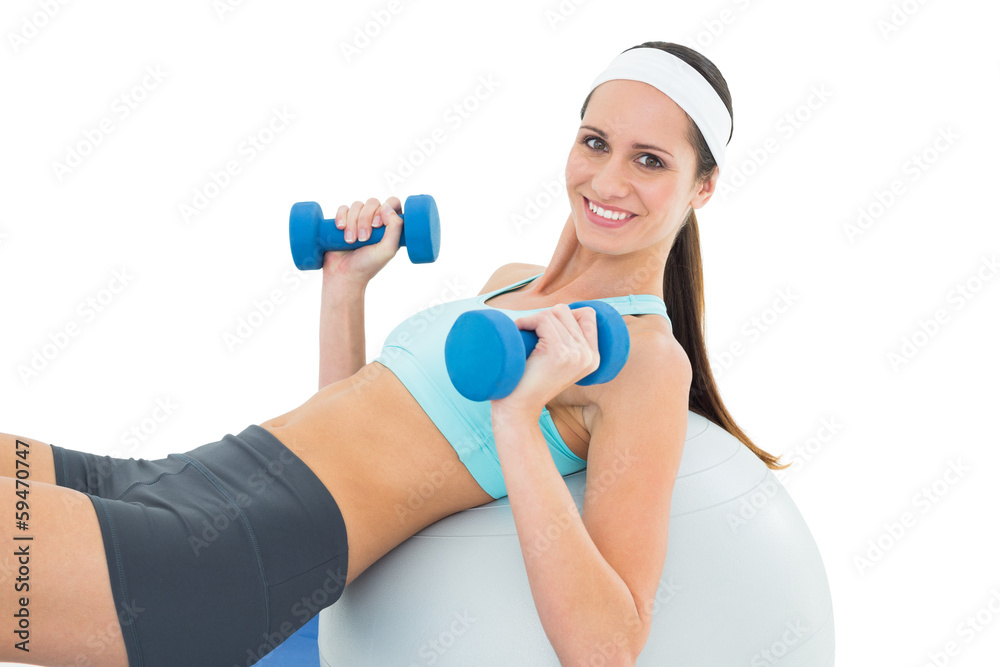 Smiling fit woman exercising with dumbbells on fitness ball Smiling fit woman exercising with dumbbells on fitness ball