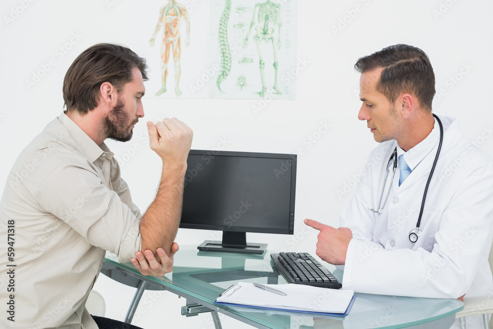 Male doctor in conversation with patient at desk Male doctor in conversation with patient at desk
