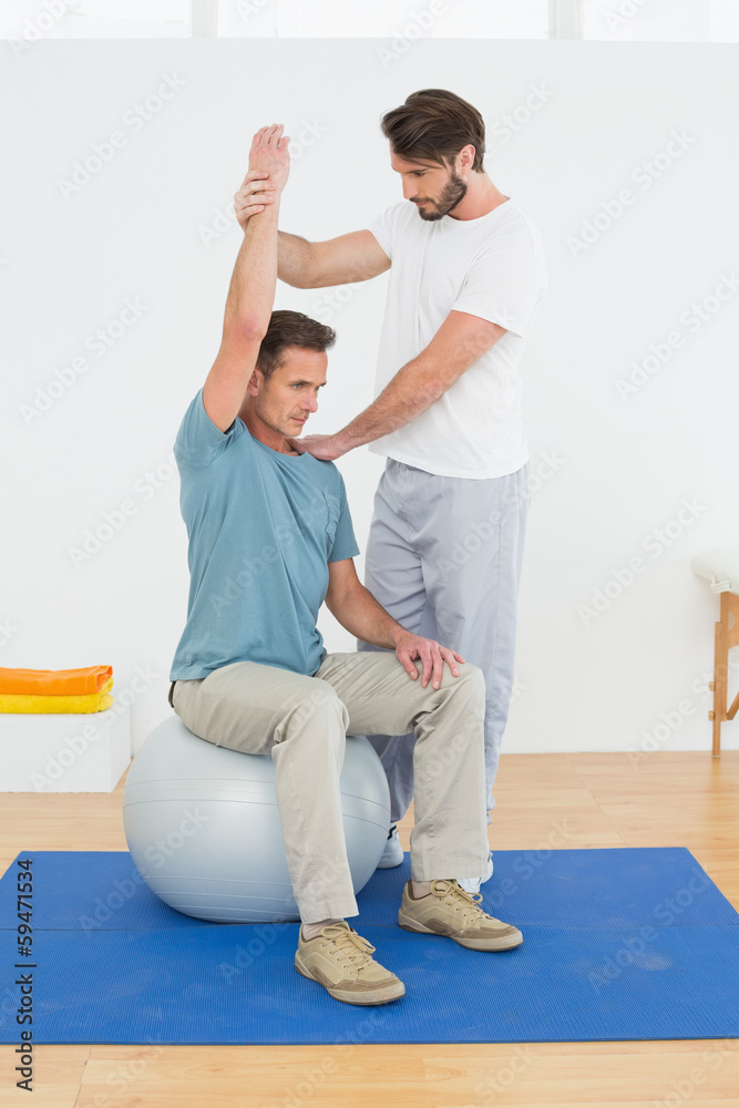 Man on yoga ball working with a physical therapist Man on yoga ball working with a physical therapist