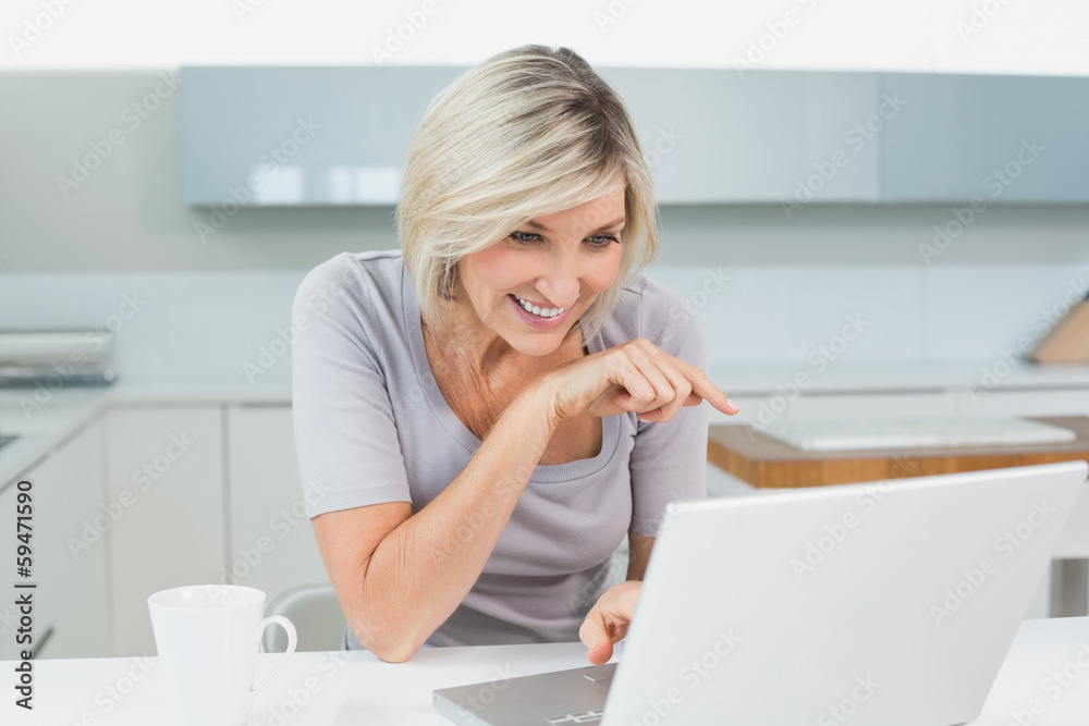 Casual woman with coffee using laptop in kitchen Casual woman with coffee using laptop in kitchen