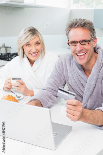 Cheerful couple in bathrobes using laptop in kitchen