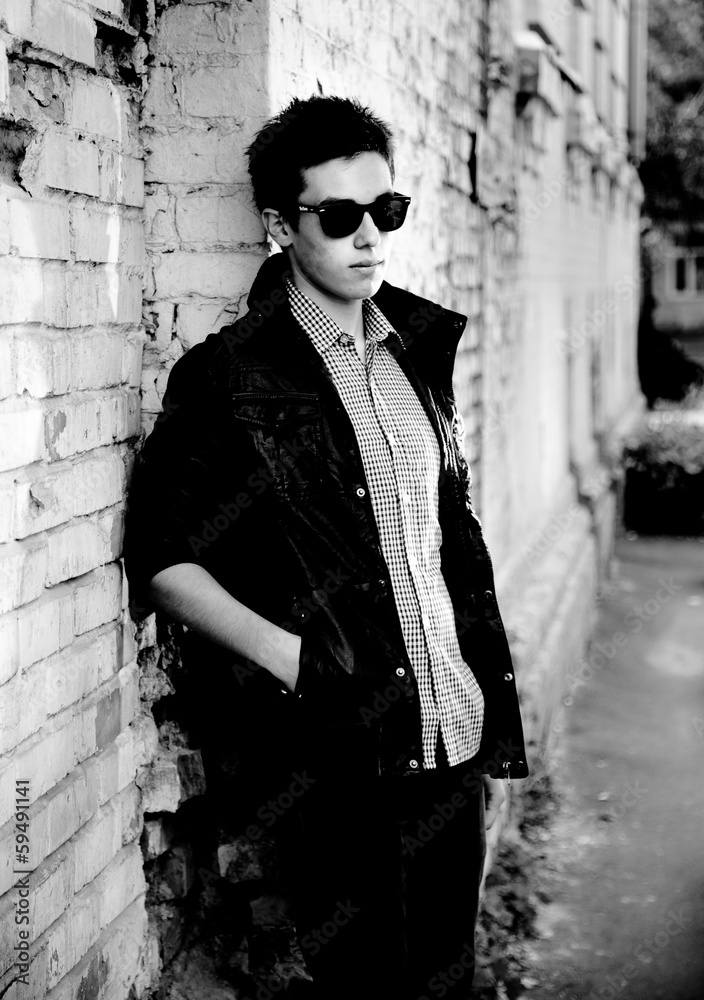 portrait of hipster boy in sunglasses leaning against brick wall