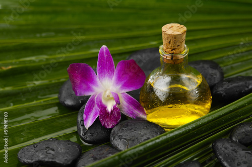 Massage oil with orchid and wet spa stones on palm leaf texture