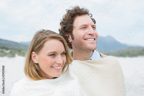 Smiling couple wrapped in blanket at beach