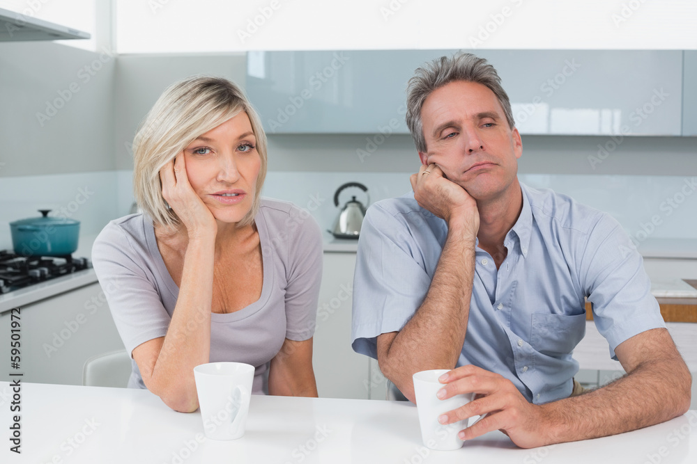Bored couple sitting with coffee cups in kitchen Bored couple sitting with coffee cups in kitchen
