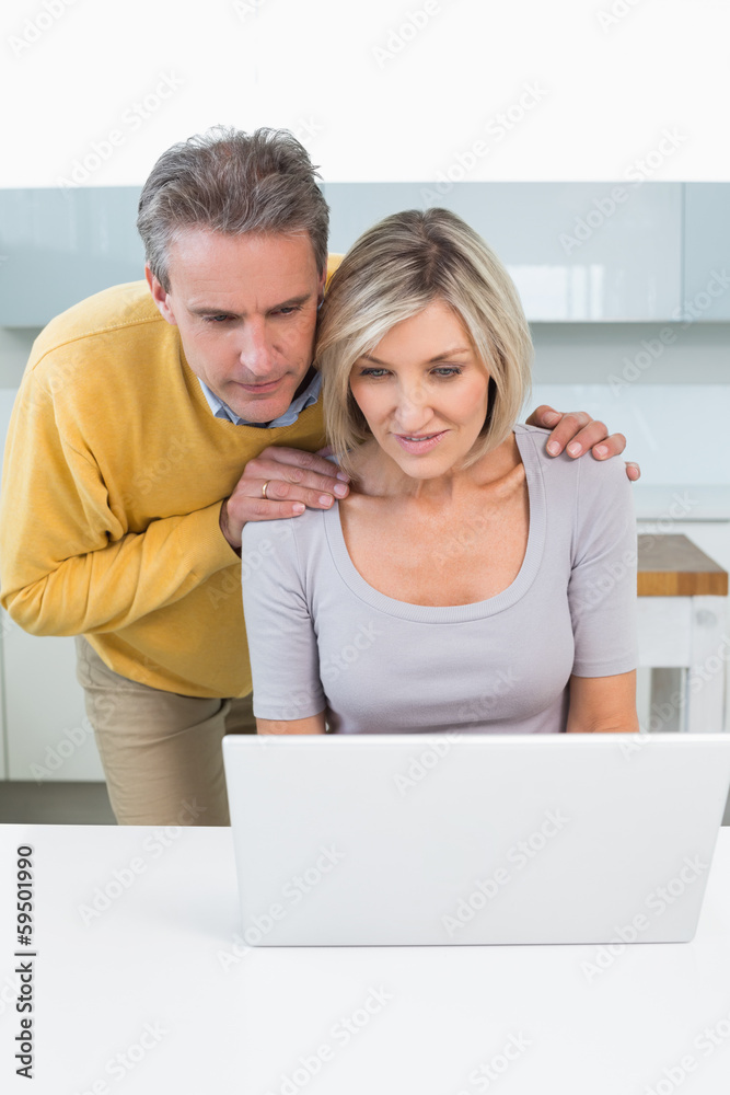 Couple looking at laptop in kitchen Couple looking at laptop in kitchen