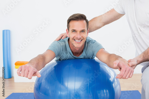 Physical therapist assisting young man with yoga ball