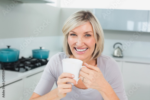 Smiling casual woman with coffee cup in kitchen