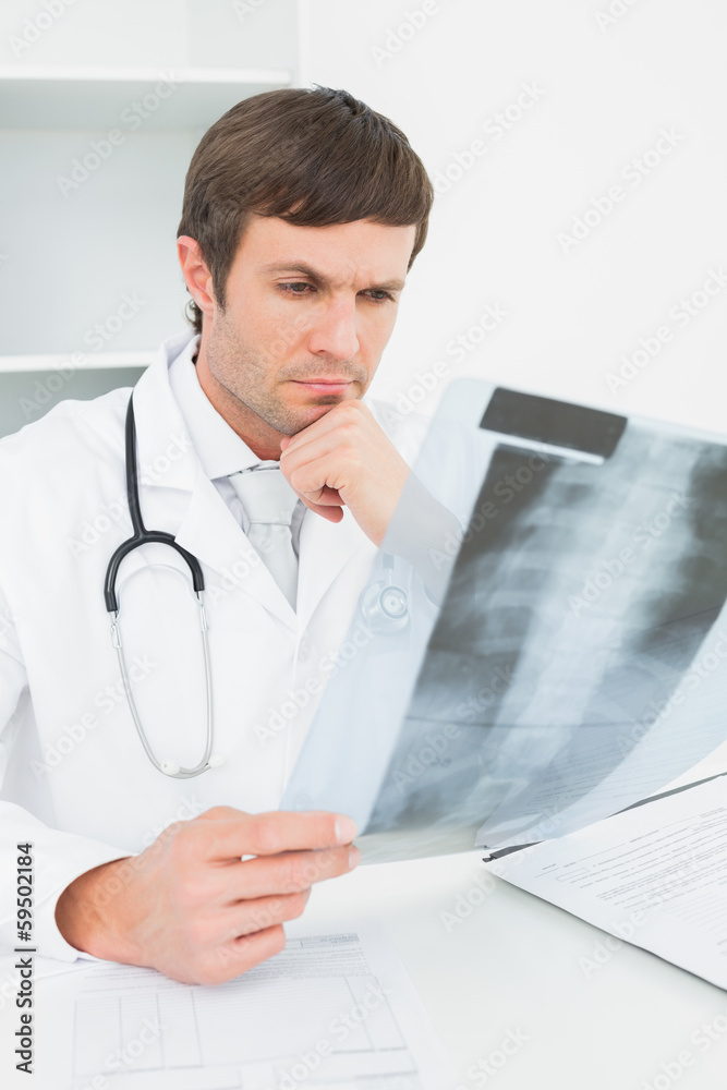 Concentrated male doctor looking at x-ray picture of spine Concentrated male doctor looking at x-ray picture of spine