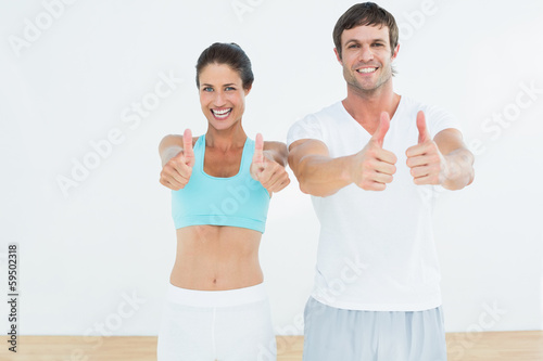 Happy fit couple gesturing thumbs up in fitness studio © lightwavemedia