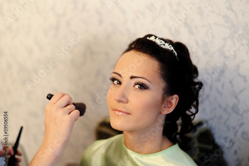 Young beautiful bride applying wedding make-up by make-up artis