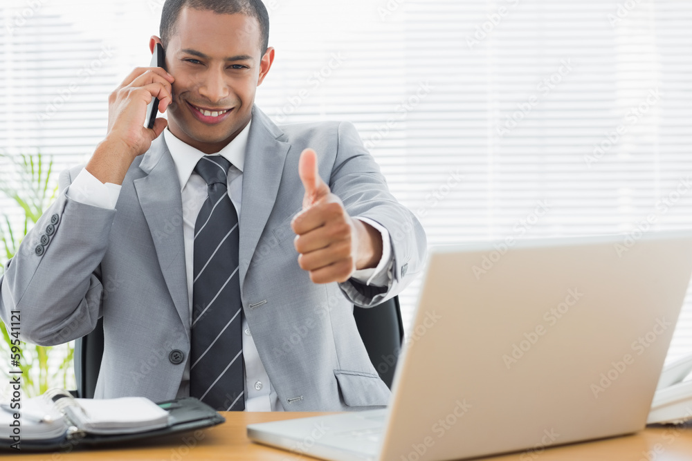 Businessman gesturing thumbs up while on call at office desk Businessman gesturing thumbs up while on call at office desk