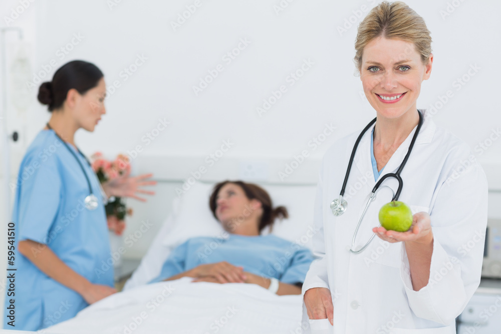 Smiling doctor holding apple with patient in hospital Smiling doctor holding apple with patient in hospital