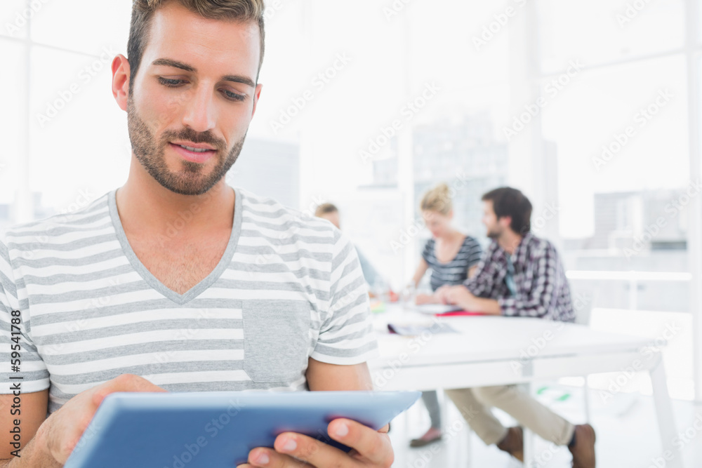 Man using digital tablet with colleagues in background Man using digital tablet with colleagues in background