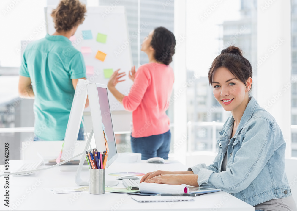 Casual woman using computer with colleagues behind in office Casual woman using computer with colleagues behind in office