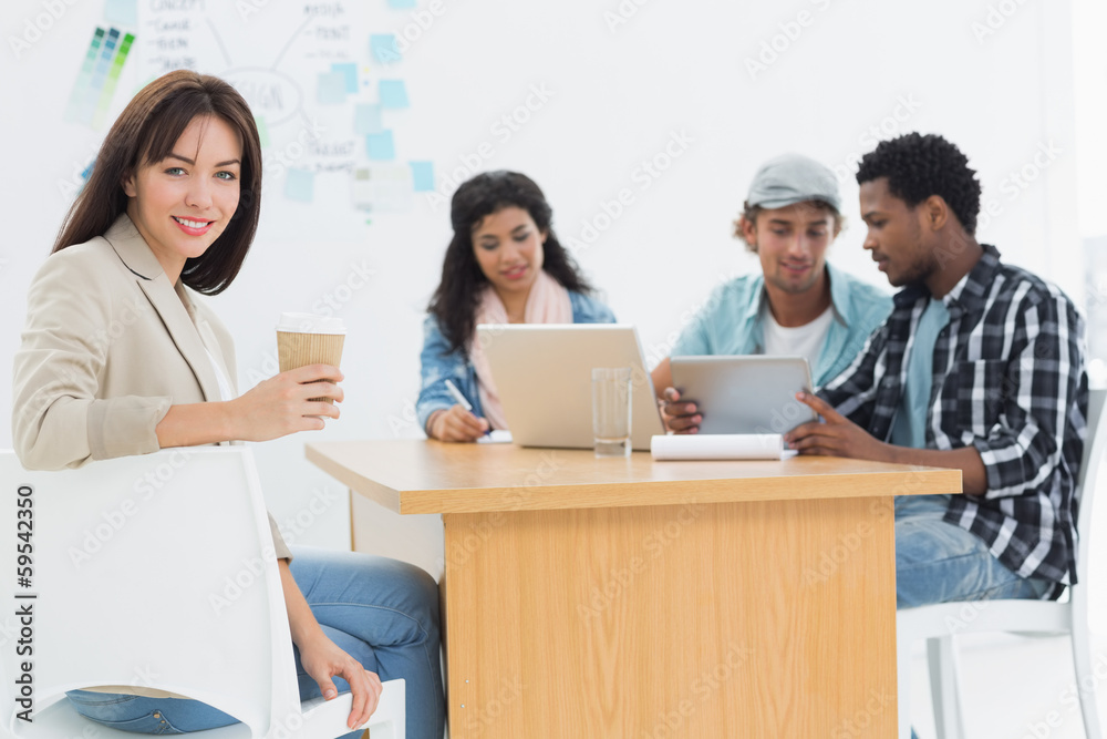 Casual woman holding take away coffee cup with colleagues behind Casual woman holding take away coffee cup with colleagues behind