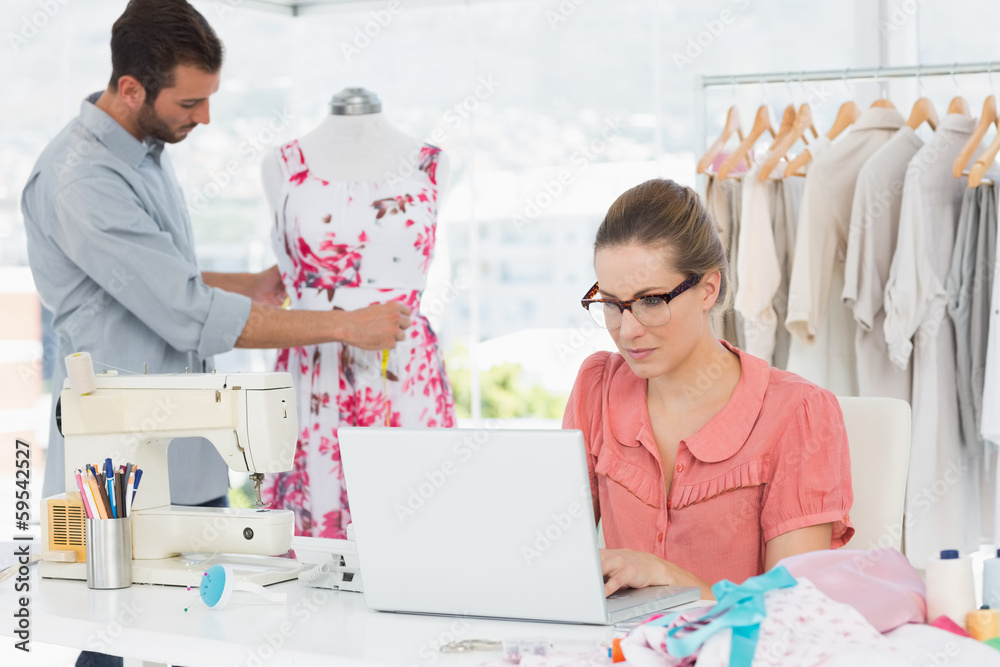 Woman using laptop with fashion designer working at studio Woman using laptop with fashion designer working at studio