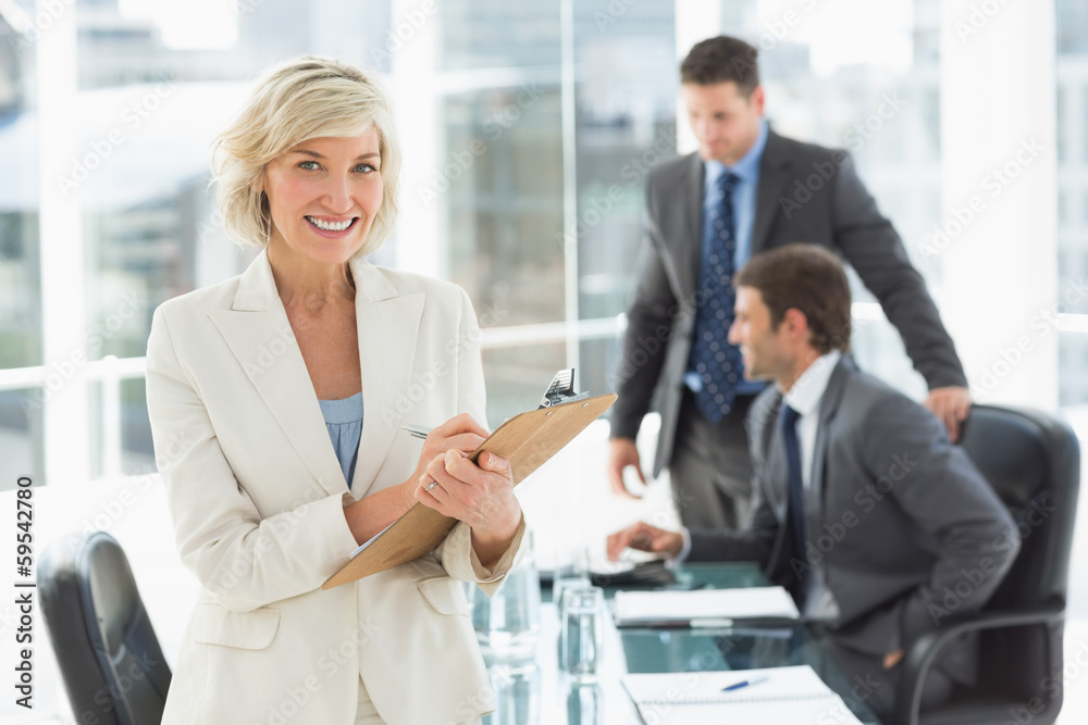 Businesswoman writing on clipboard with colleagues in background Businesswoman writing on clipboard with colleagues in background