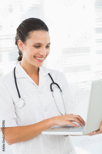 Concentrated smiling female doctor using laptop