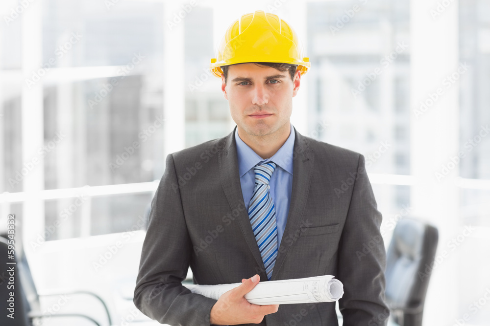 Serious architect holding blueprints looking at camera Serious architect holding blueprints looking at camera