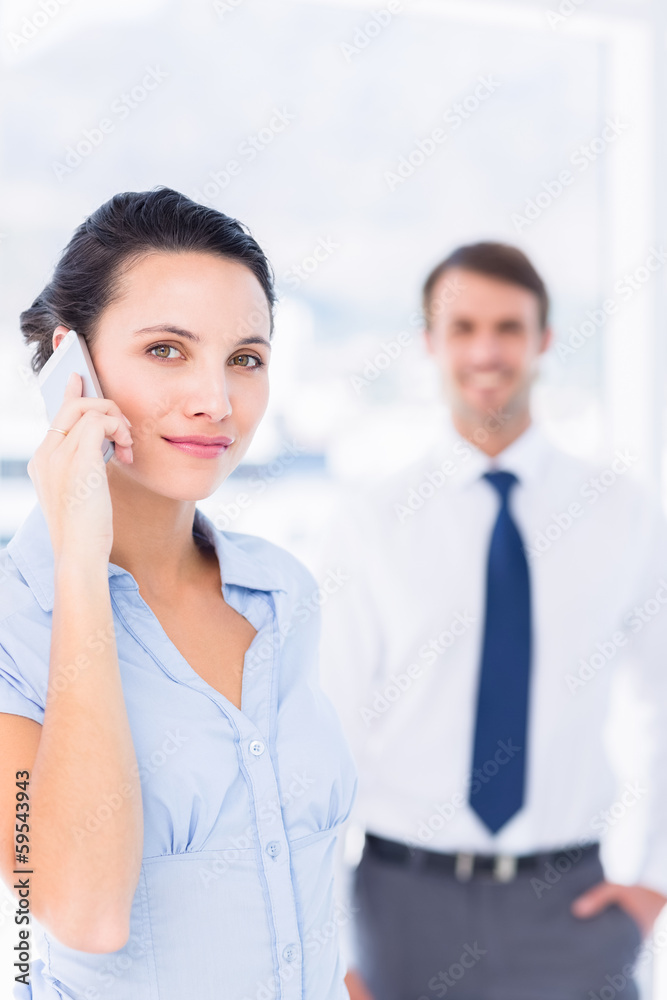 Woman on call with male colleague in background Woman on call with male colleague in background
