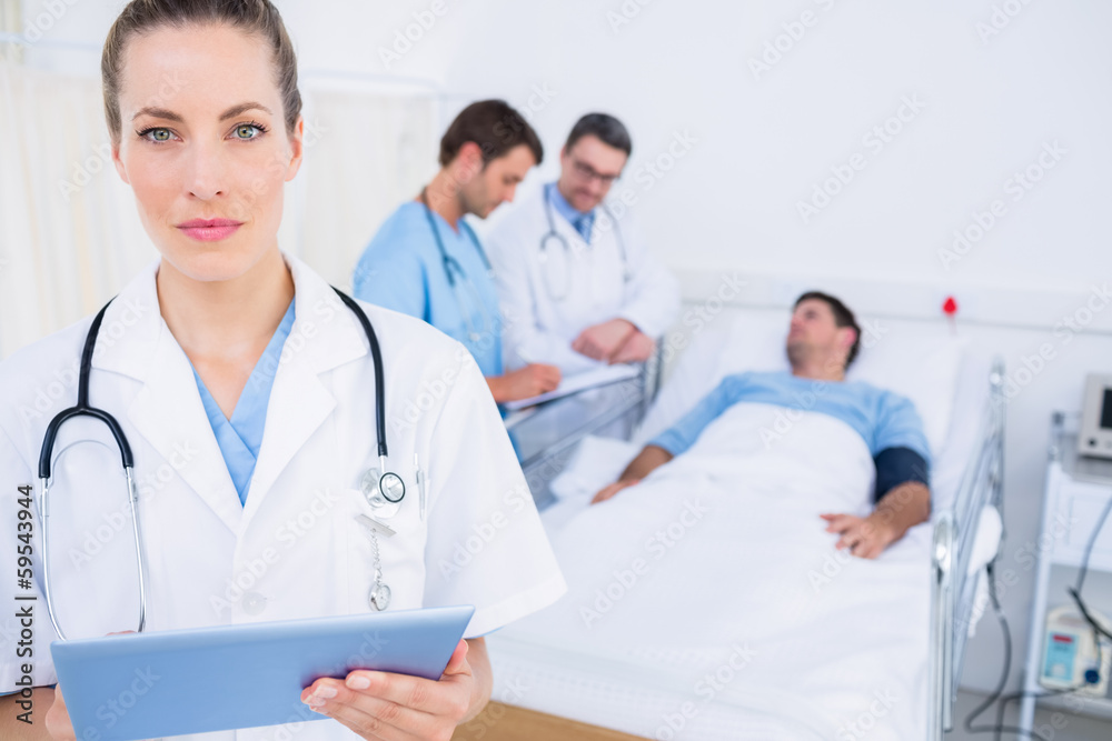 Doctor using digital tablet with colleagues and patient behind Doctor using digital tablet with colleagues and patient behind