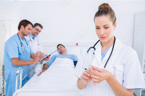 Doctor holding syringe with colleagues and patient at hospital