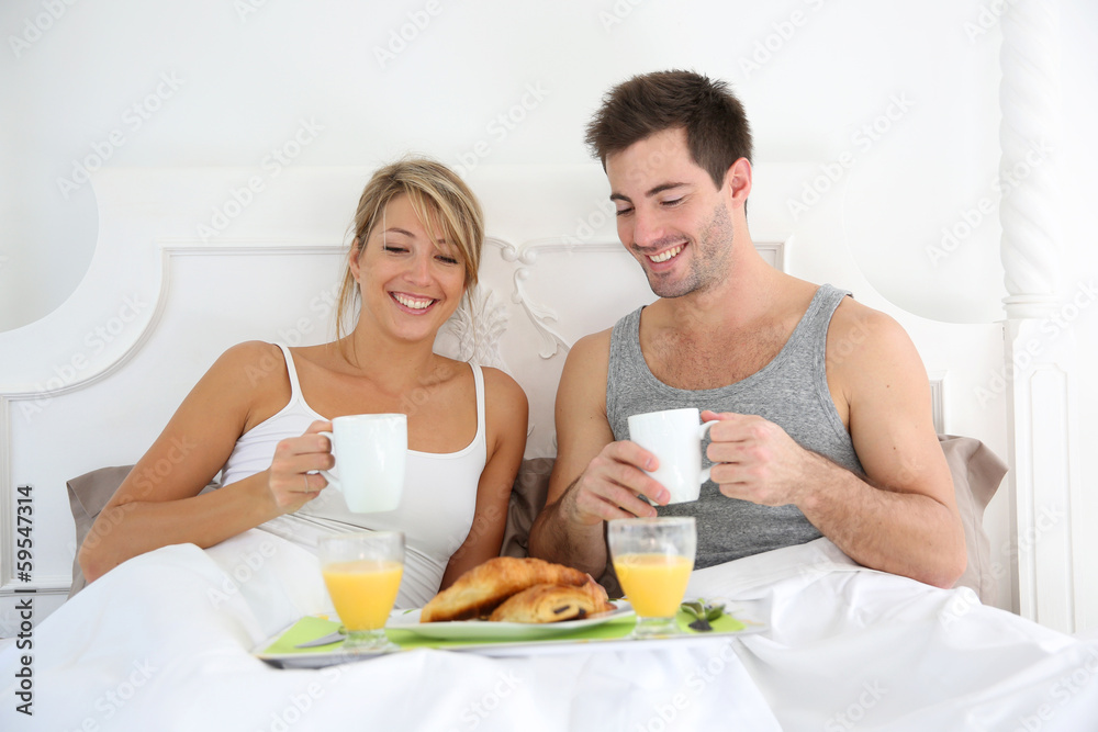 Cheerful young couple having breakfast in bed