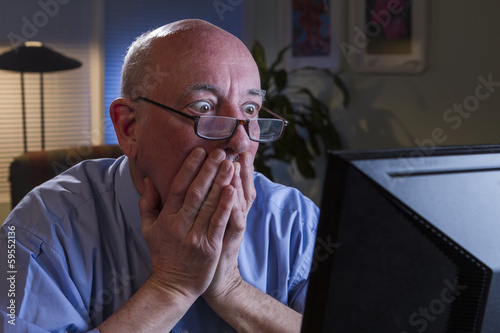 Older man shocked as he reads his computer monitor, horizontal