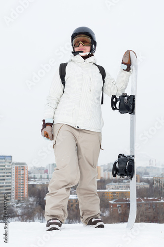 girl snowboarder in helmet stands on hill with snowboard photo