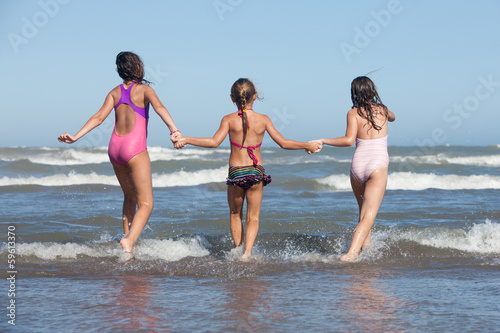 three happy girls running into the ocean